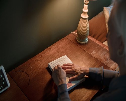 Person reading a book under a warm desk lamp at night
